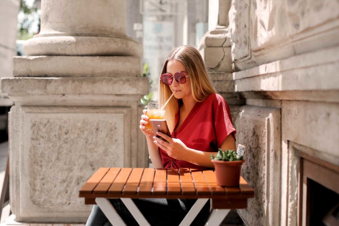 Jeune femme buvant sur un terrasse et utilisant son téléphone, carte sim albanie